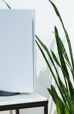 Playstation 5 Die PlayStation 5 steht dekorativ auf einem Marmortisch neben einer Zimmerpflanze. An die Konsole angelehnt steht der neue DualSense-Controller.