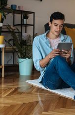 Thread Eine Person sitzt auf einem Teppich und hält ein Tablet in der Hand.
