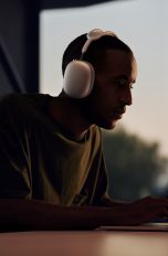 Apple One Eine Person mit Apple AirPods Max sitzt vor einem MacBook.