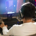 Eine Person mit einem Headset auf dem Kopf sitzt vor einem Rechner und spielt etwas.