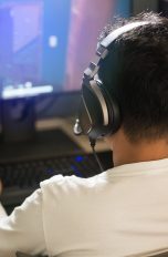 Capture Cards Eine Person mit einem Headset auf dem Kopf sitzt vor einem Rechner und spielt etwas.