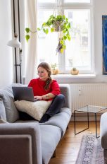 DSL, TV-Kabel & Glasfaser Eine Frau sitzt mit ihrem Laptop auf dem Sofa in ihrem Wohnzimmer.