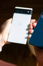 Android Wechsel iPhone Zwei Hände halten jeweils ein Smartphone: Einmal ein weißes Google Phone und einmal ein dunkelblaues iPhone.