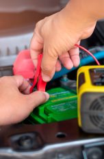 Eine Person steckt ein Batterieladegerät an eine Autobatterie an.