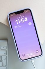 Ein iPhone 13 liegt zwischen mehreren Deko-Elementen und wird über ein Lightning-Kabel aufgeladen. Ein iPhone 13 liegt zwischen mehreren Deko-Elementen und wird über ein Lightning-Kabel aufgeladen.