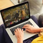 Eine Person sitzt mit einem Laptop auf dem Scho&szlig; auf einem Sofa. Auf dem Bildschirm ist die Netflix-Hauptseite zu sehen.
