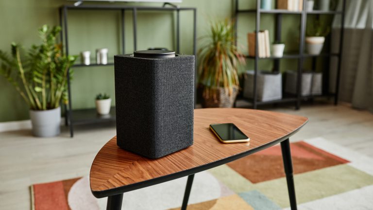 Auf einem Couchtisch in einem Wohnzimmer steht ein Lautsprecher, neben dem ein Smartphone liegt.