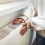 Eine Person h&auml;lt beide H&auml;nde an einen Heizk&ouml;rper, der an einer Wand angebracht ist.