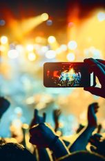 Fotos wiederherstellen bei Android, So geht’s Eine Person hält ein Smartphone horizontal in die Höhe, um ein Foto von einer Bühne zu schießen auf der ein Konzert stattfindet.