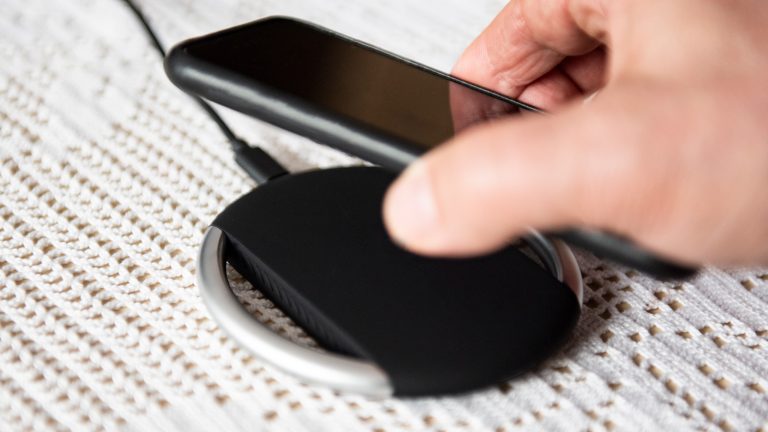 Ideen fürs Wichtelgeschenk, Technik-Gadgets unter 15, 25 und 50 Euro Nahaufnahme eines kabellosen Ladepads. Die Hand einer Person ist gerade dabei ein Smartphone darauf zu legen.